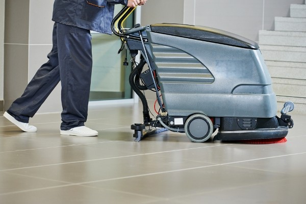 Medewerker die een kantoorvloer reinigt met een professionele schrobmachine